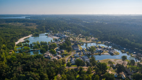 Luchtbeeld van een glamping site tussen bossen, met huisjes rond vijvers in een groene omgeving.