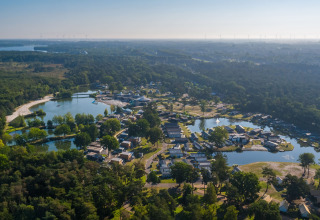 Luchtbeeld van een glamping site tussen bossen, met huisjes rond vijvers in een groene omgeving.