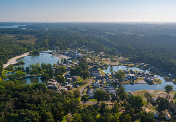 Luftfoto af et glamping-resort omgivet af skov, søer og hytter spredt ud i det naturskønne område.