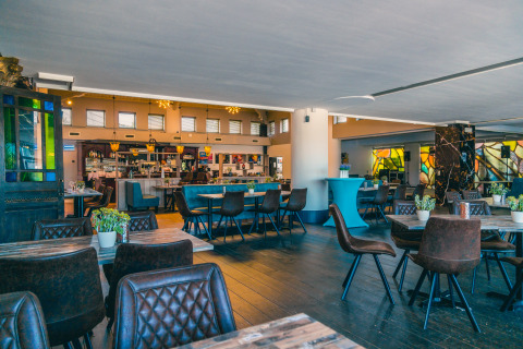 Licht, eigentijds restaurant bij een glampingverblijf met houten tafels, leren stoelen en planten.