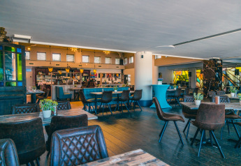 Lys og moderne restaurant med træmøbler, læderstole og grønne planter på glampingresort.