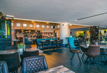 Lys og moderne restaurant med træmøbler, læderstole og grønne planter på glampingresort.