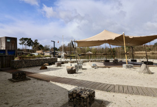 Glampinglocatie met zand, houten paden, tentoverkapping en uitzicht op een prachtig bosrijk meer.