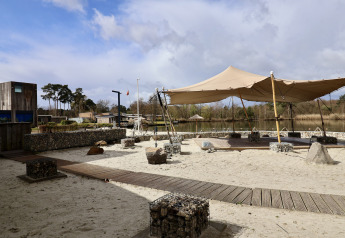 Luksus glampingområde med telt og sand omgivet af natur, træer og sø under en overskyet himmel.