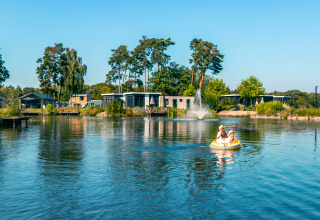 Hébergement glamping avec cabanes modernes au bord d’un lac, deux personnes pagaient en bateau gonflable.