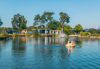 Glamping-indkvartering med moderne hytter ved en sø, to personer sejler i en oppustelig båd på vandet.
