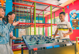 Kinderen en volwassenen amuseren zich samen met tafelvoetbal in een kleurrijke glamping speeltuin.