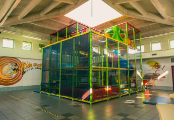 Parque infantil interior con estructura para escalar y toboganes en un glamping, sala luminosa con dibujos.