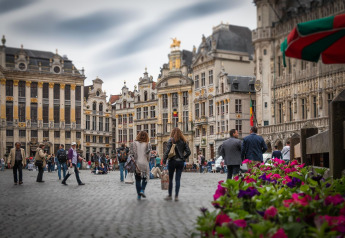Folk spadserer på en smuk historisk plads med farverige blomster og udsmykkede bygninger i Bruxelles.