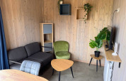 Moderne opholdsstue i Mobi Lodge på Arden Parks Tulderheyde, Belgien, med træpaneler og stilfulde møbler.