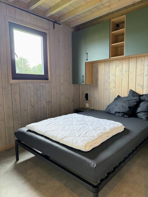 Camera moderna in legno con letto nero e finestra, fotografata alla Mobi Lodge, Arden Parks Tulderheyde.