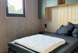 Camera moderna in legno con letto nero e finestra, fotografata alla Mobi Lodge, Arden Parks Tulderheyde.