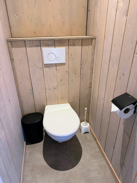 Bagno moderno con pannelli in legno, sciacquone a parete e scopino a Mobi Lodge, Arden Parks Tulderheyde, Belgio.