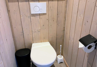 Bagno moderno con pannelli in legno, sciacquone a parete e scopino a Mobi Lodge, Arden Parks Tulderheyde, Belgio.