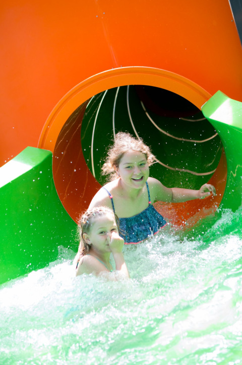 Deux enfants heureux arrivent dans l'eau après un toboggan coloré dans un site de glamping.