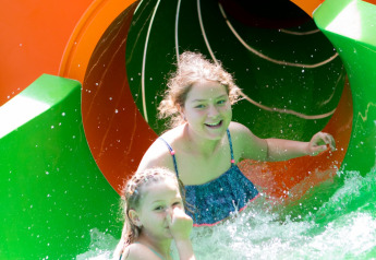 Zwei lachende Kinder kommen aus einer bunten Wasserrutsche in einem Glamping-Resort ins Wasser.