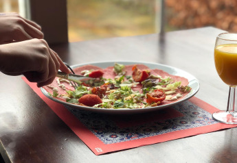 Eine Person schneidet Essen auf einem Teller mit Salat und Tomaten neben einem Glas Saft im Glamping-Quartier.