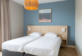 Lodge room with two single beds, a blue accent wall, wooden headboard, and minimalist decor elements.