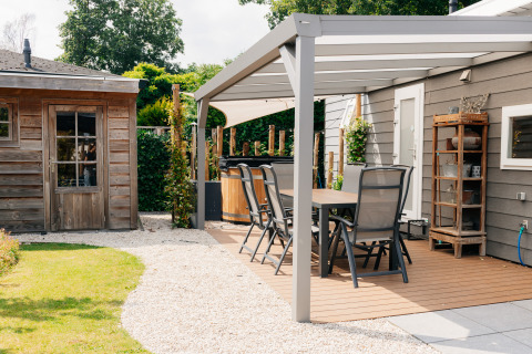 Veluwelodge XL terras met hot tub, tuinhuisje en eettafel in een rustgevende tuinomgeving.