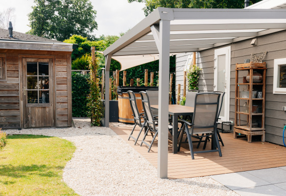 Veluwelodge XL terras met hot tub, tuinhuisje en eettafel in een rustgevende tuinomgeving.
