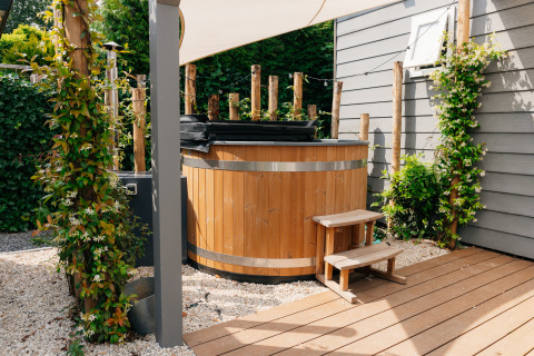 Houten buitenjacuzzi met trapje bij Veluwelodge XL in De Boshoek, Nederland, omringd door beplanting.