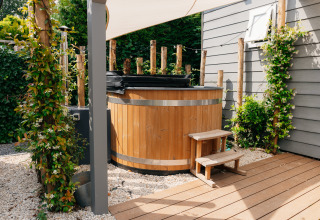 Houten buitenjacuzzi met trapje bij Veluwelodge XL in De Boshoek, Nederland, omringd door beplanting.