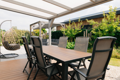 Buitenterras bij Veluwelodge XL op De Boshoek in Nederland met eettafel, stoelen en een hangstoel.