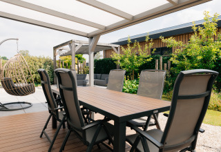 Buitenterras bij Veluwelodge XL op De Boshoek in Nederland met eettafel, stoelen en een hangstoel.