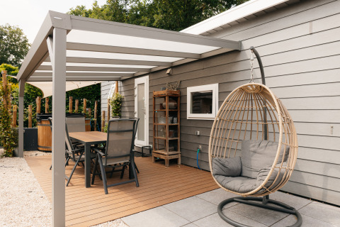 Buitenterras aan Veluwelodge XL in De Boshoek, Nederland, met eettafel en hangstoel onder een overkapping.