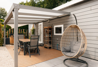 Buitenterras aan Veluwelodge XL in De Boshoek, Nederland, met eettafel en hangstoel onder een overkapping.