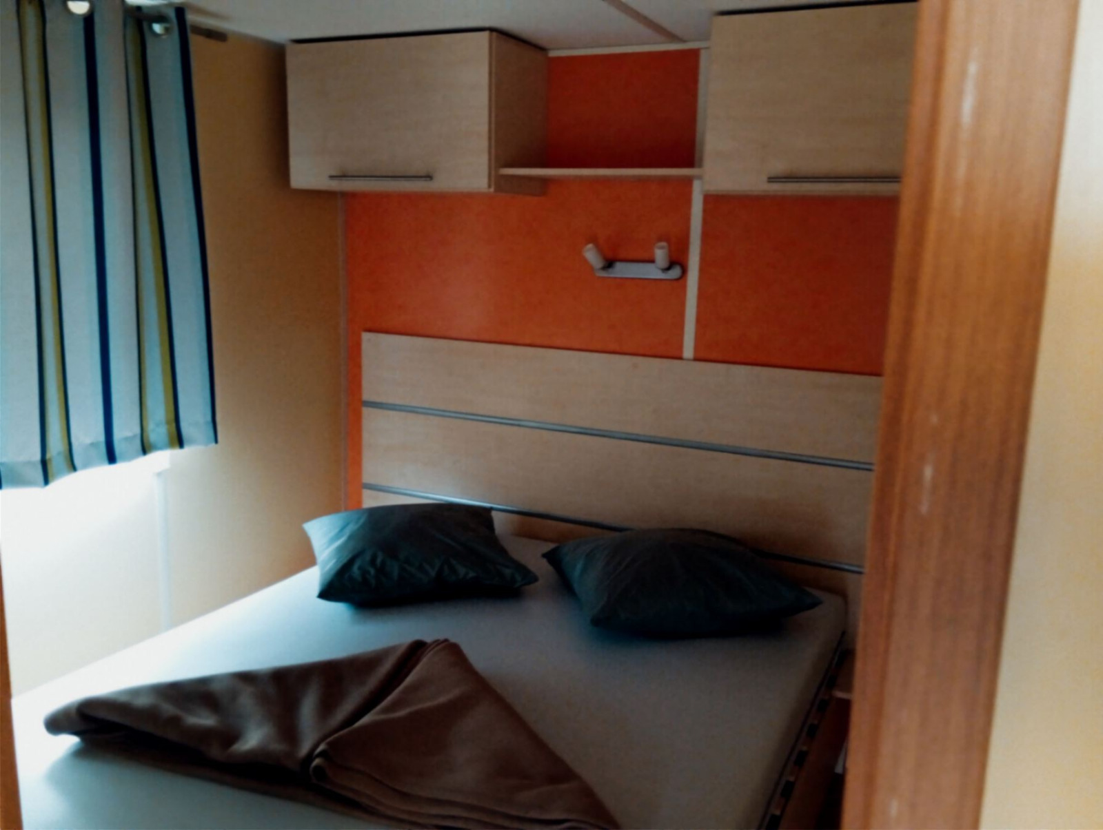 Slaapkamer in Mobile Home Comfort op Camping Seasonova Sous le Moulin met bed, kussens en kast.