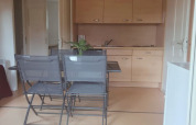 Angolo cucina luminoso con mobili in legno e tavolo da pranzo nel Chalet Eco di Camping Paradis Les Chanterelles, Francia.