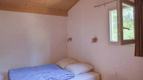 Camera semplice con letto matrimoniale, finestra aperta e soffitto in legno al Chalet Eco, Camping Paradis Les Chanterelles.