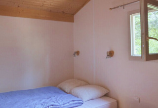 Camera semplice con letto matrimoniale, finestra aperta e soffitto in legno al Chalet Eco, Camping Paradis Les Chanterelles.