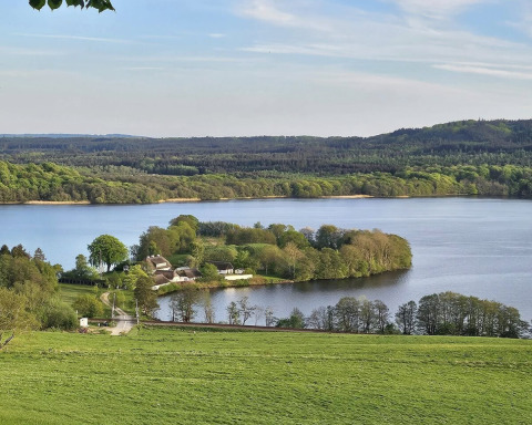 Landschap nabij Silkeborg, Denemarken, met meer, groene velden en omliggend bos in het zonlicht.
