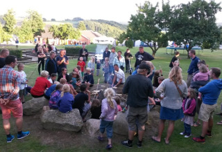 Een grote groep mensen verzamelt zich rond een kampvuur op Terrassen Camping in Centraal-Denemarken.
