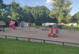 Speeltuin met glijbaan en schommels bij Terrassen Camping, Centraal Denemarken, omgeven door caravans en bomen.