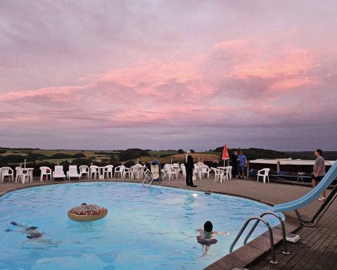 Udendørs swimmingpool ved Terrassen Camping i Danmark med folk, hvide stole og smuk lyserød himmel.
