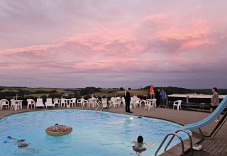 Udendørs swimmingpool ved Terrassen Camping i Danmark med folk, hvide stole og smuk lyserød himmel.