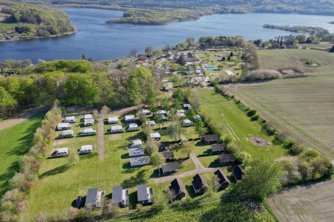 Luchtfoto van Terrassen Camping in Midden-Denemarken met huisjes, caravans en uitzicht op een meer.