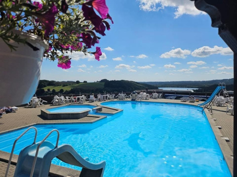 Outdoor swimming pool with waterslide at Terrassen Camping, overlooking hills and a lake in Central Denmark.