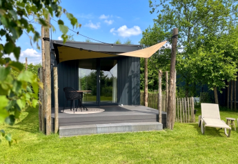 Tiny house moderne avec bain extérieur, terrasse et transats sur pelouse verdoyante et ciel bleu.