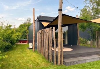 Tiny House à De Kremmer, aux Pays-Bas, avec terrasse en bois, voile d’ombrage et jardin verdoyant.