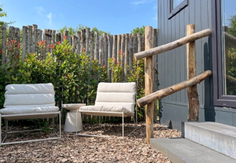 Coin salon extérieur au Tiny House de De Kremmer, Pays-Bas, avec deux fauteuils, une table et une clôture en bois.