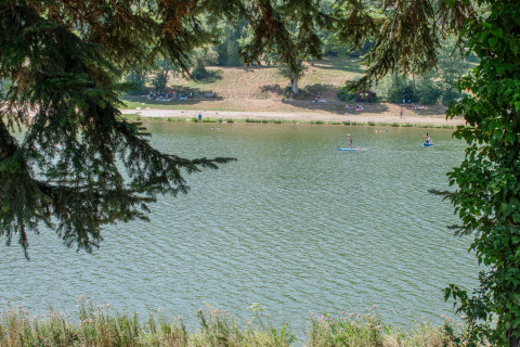 Blick auf den See beim Onlycamp Camping Le Lac de Roybon mit SUP-Fahrern und entspannenden Menschen am Ufer.