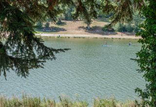 Vue sur le lac au Onlycamp Camping Le Lac de Roybon, personnes faisant du paddle et se relaxant sur la rive.