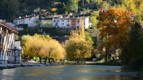 Fluss und herbstliche Bäume in Roybon, Auvergne-Rhône-Alpes, Frankreich, mit Häusern auf einem Hügel.
