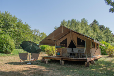 Tenda safari Ponza con veranda coperta, sedie e ombrellone, immersa nel verde della natura e degli alberi.