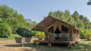 Tenda safari Ponza con veranda coperta, sedie e ombrellone, immersa nel verde della natura e degli alberi.