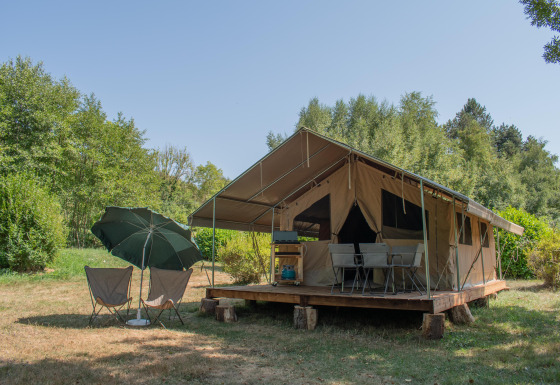 Tenda safari Ponza con veranda coperta, sedie e ombrellone, immersa nel verde della natura e degli alberi.